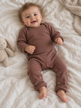 Baby im Merino-Einteiler in Zimt liegt lachend auf einer Decke, Ansicht von oben